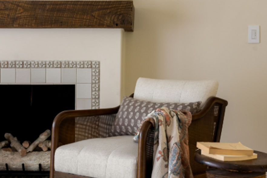 Living room armchair beside a fireplace, with a draped blanket and books on a side table