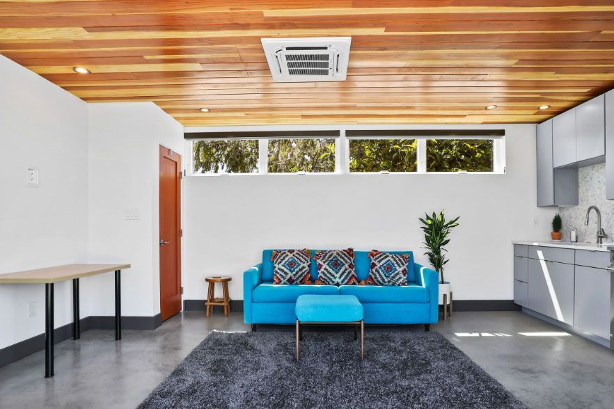 Modern living room with blue sofa, gray rug, wood ceiling, and open kitchen area