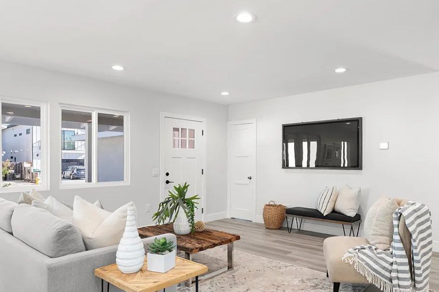 Bright modern living room with white walls, gray sofa, black bench, and wooden coffee tables