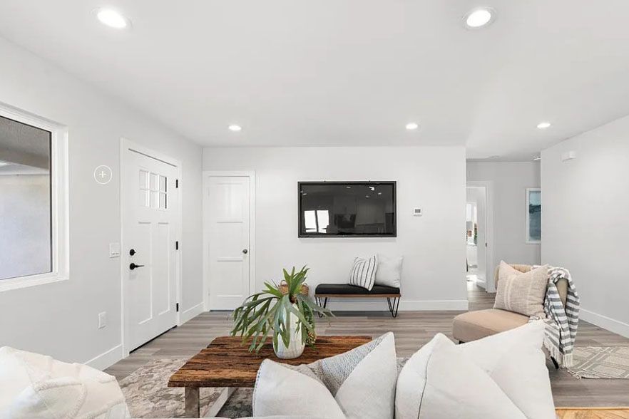 Bright white living room with sectional sofa, wall-mounted TV, coffee table, and wood floors