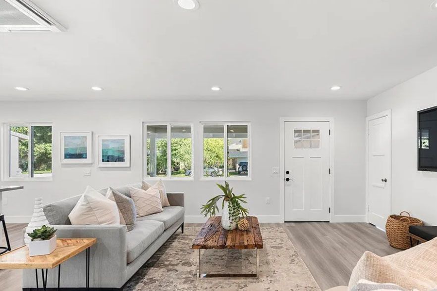 Bright modern living room with white walls, gray sofa, coffee table, and large windows