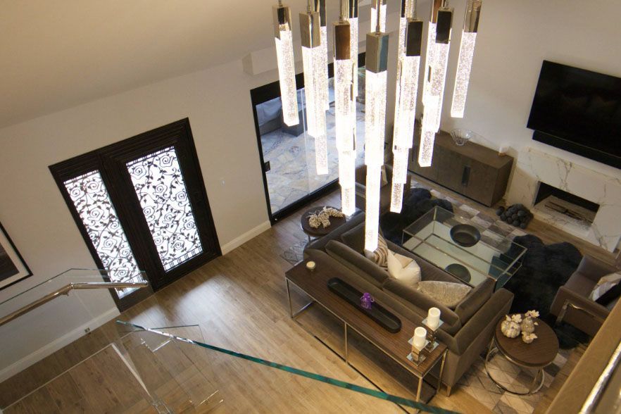 Modern living room with chandelier, glass coffee table, sofa, wall TV, and double front doors