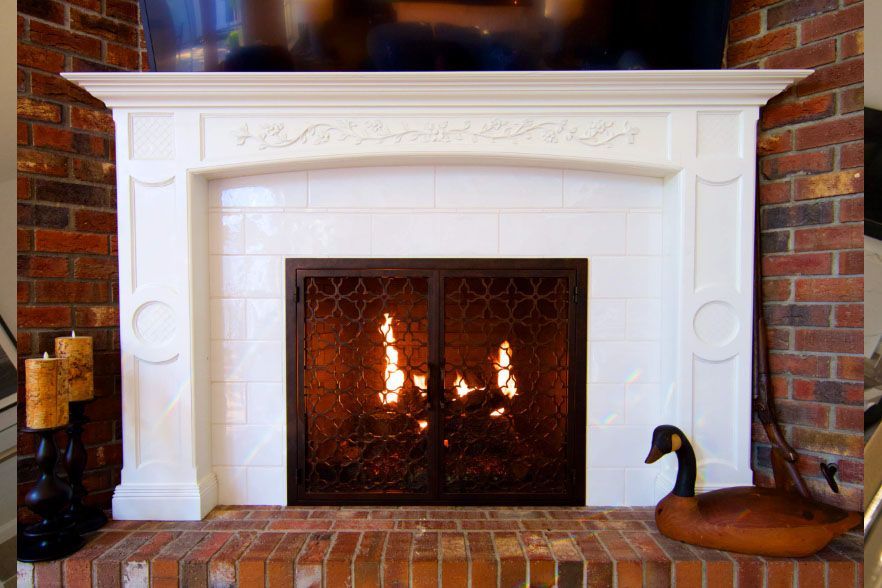 White fireplace with a lit fire, brick hearth, and a black duck figurine on the right.
