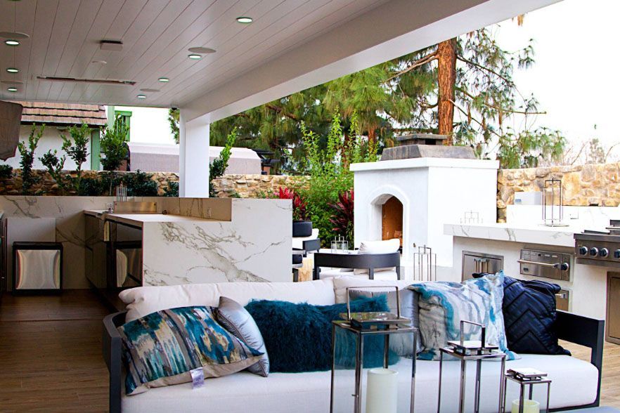 Modern patio lounge with white sofas, blue pillows, and a small fireplace under a covered terrace