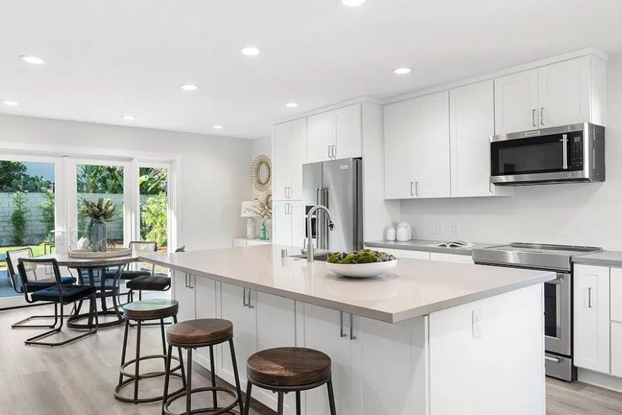 Bright modern white kitchen with island, bar stools, and dining area by large glass doors