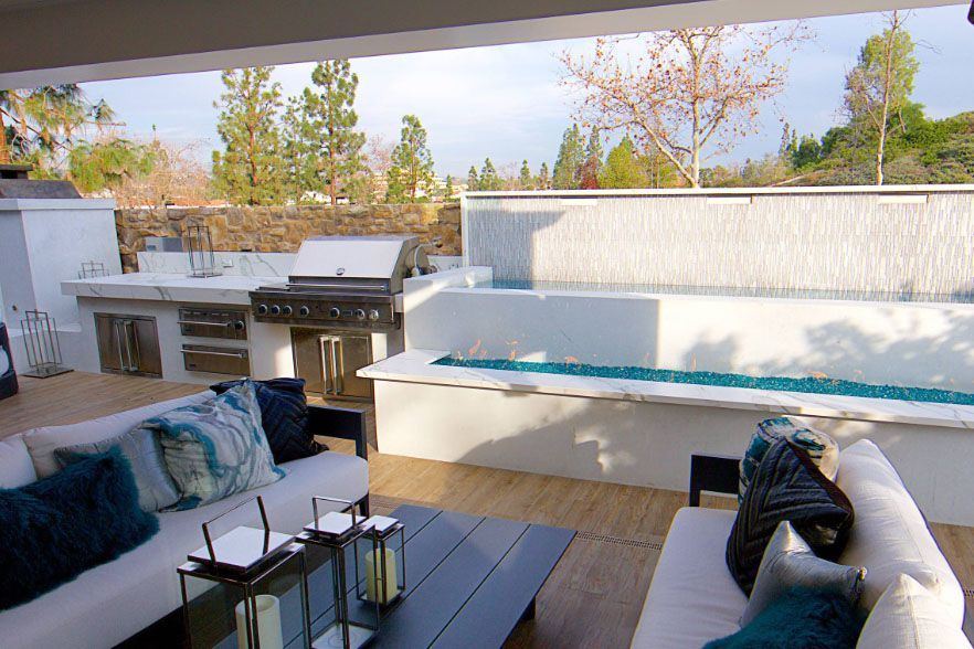 Modern patio with white seating, outdoor grill, and black coffee table in a sunny backyard.