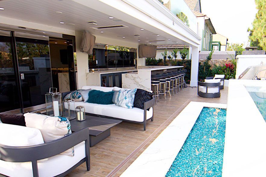 Modern patio with lounge seating, bar stools, and a narrow turquoise pool under a white pergola.