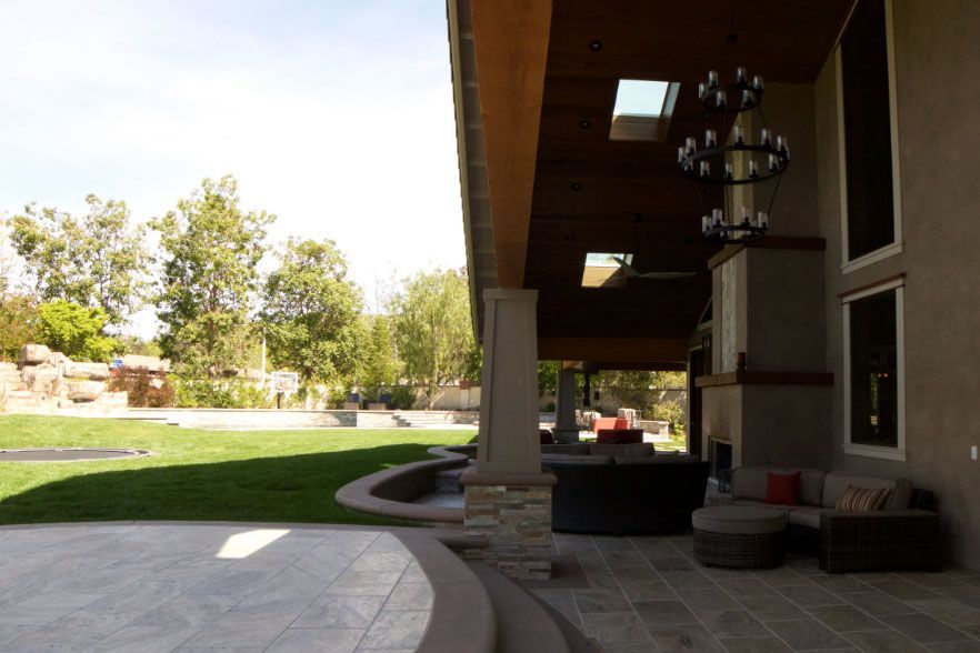 Covered patio with stone columns and wicker seating beside a grassy courtyard and trees