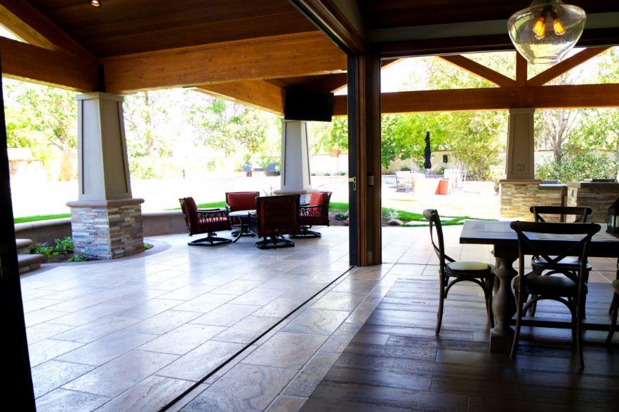 Covered patio with dark wood beams, tile floor, and outdoor seating overlooking a bright garden.