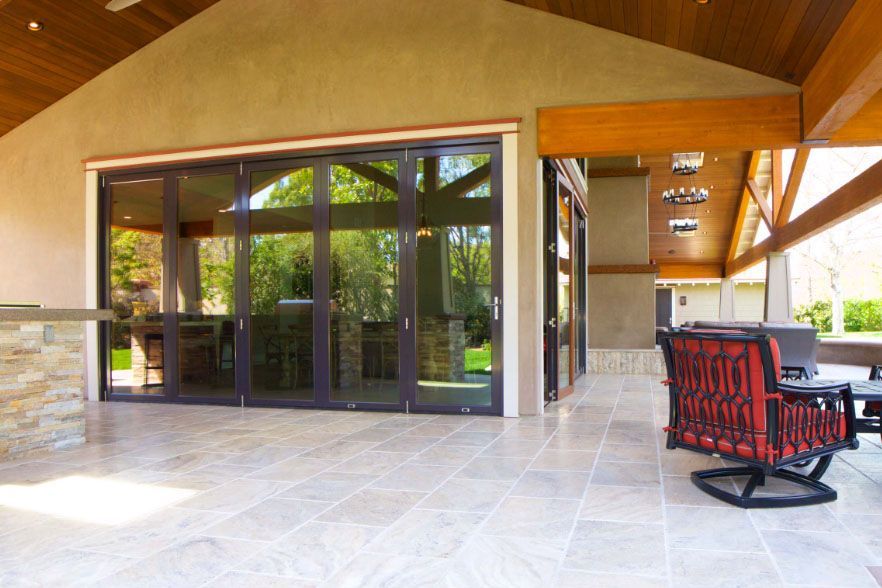 Covered patio with stone floor, wood ceiling, glass doors, and red cushioned rocking chair