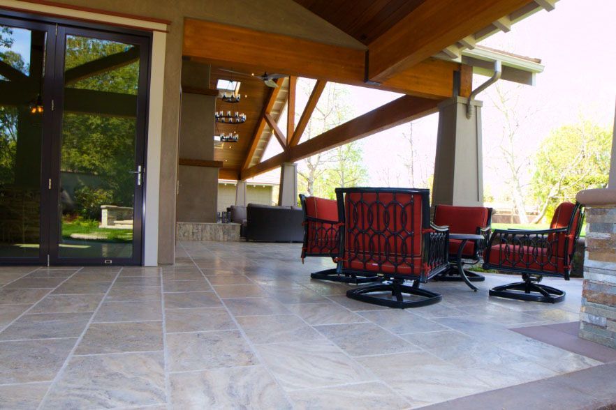 Covered patio with red cushioned seating, stone tile floor, and a wooden staircase