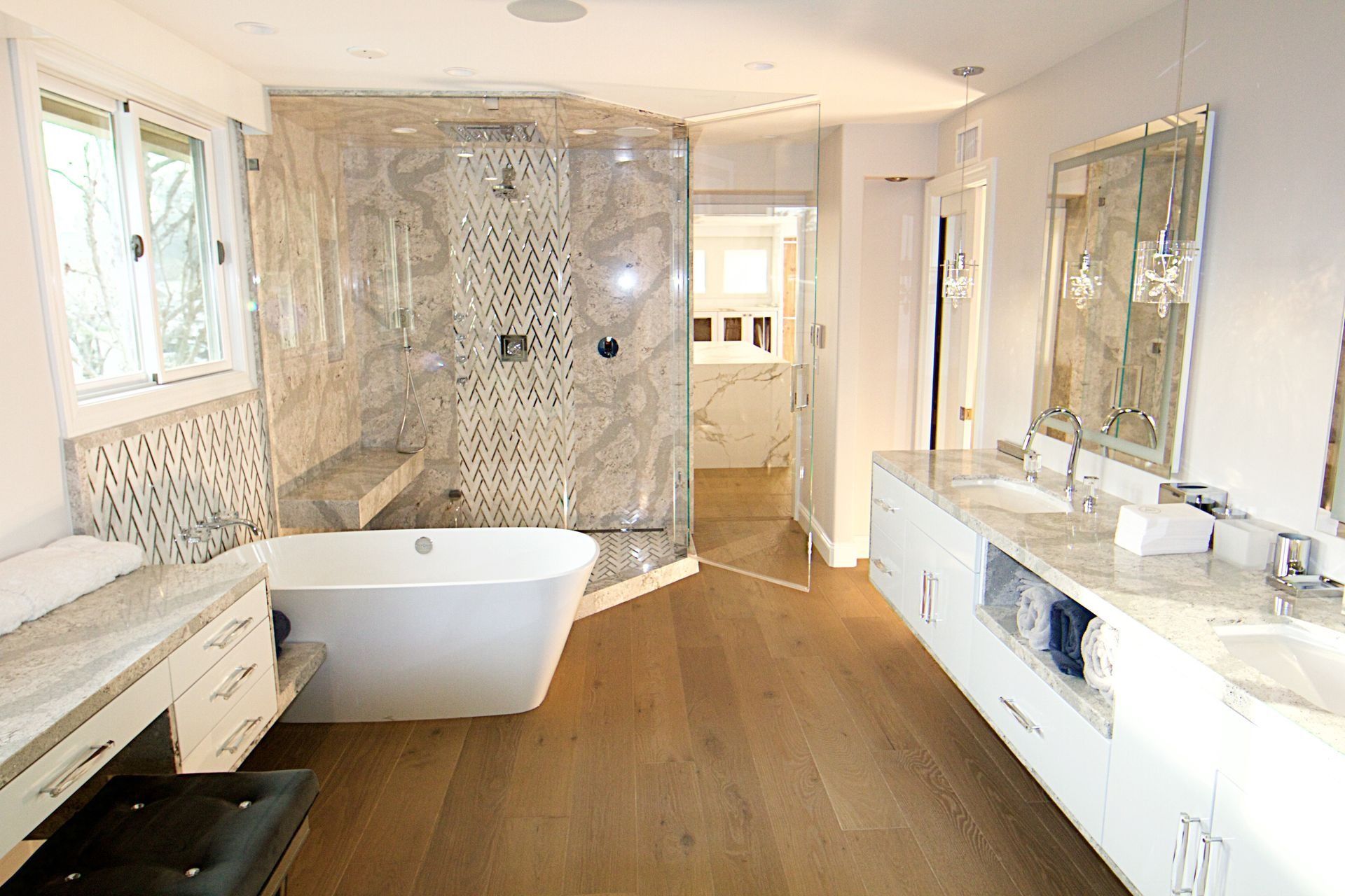 A modern, white-themed bathroom featuring a freestanding tub, tiled glass shower, double vanity, and hardwood flooring.