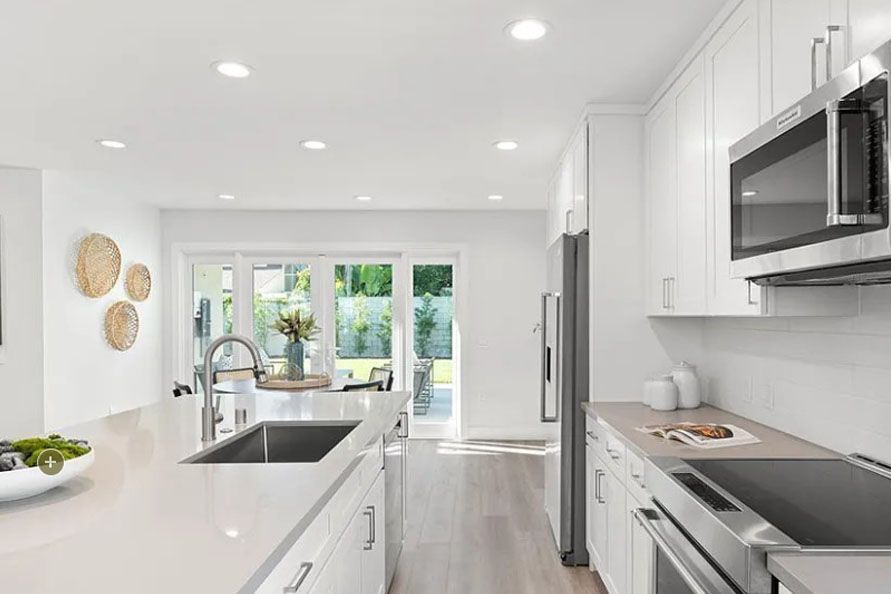 Bright white modern kitchen with island, stainless appliances, and large windows overlooking greenery