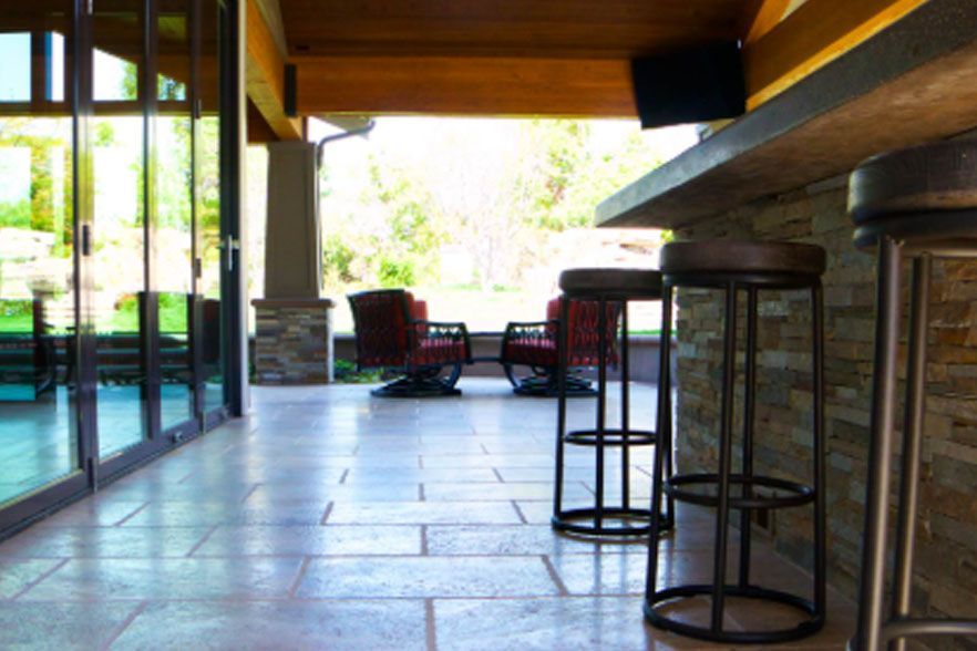 Covered patio with tiled floor, stone wall, and tall bar stools near glass doors