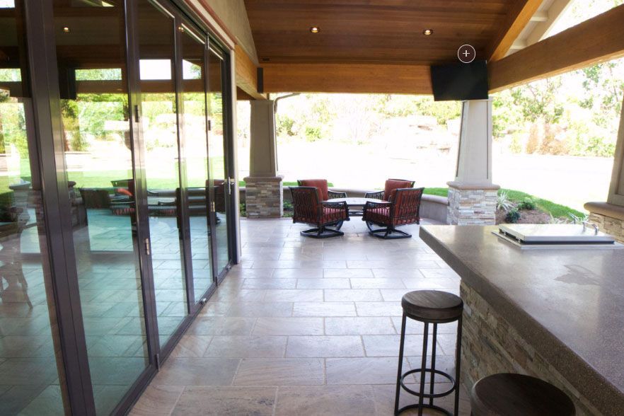 Covered patio with sliding glass doors, stone floor, bar counter, and outdoor seating overlooking a bright yard