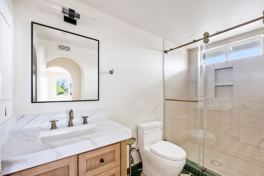 Bright bathroom with white vanity, mirror, toilet, and glass shower enclosure