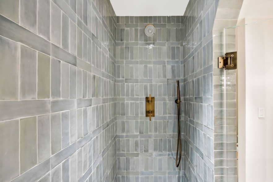 Empty tiled shower with gray walls, brass fixtures, and a handheld showerhead