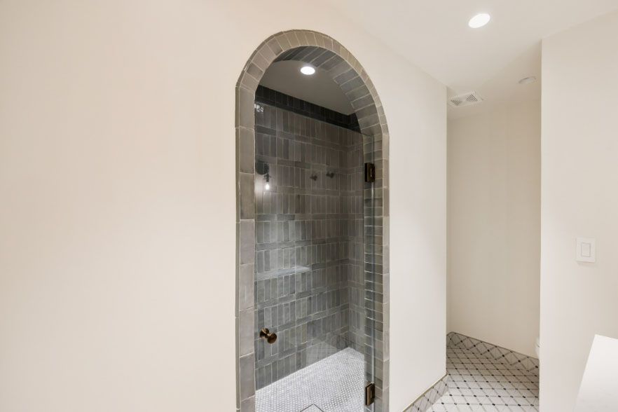 Arched tiled shower stall in a bright bathroom with white walls and patterned floor tiles