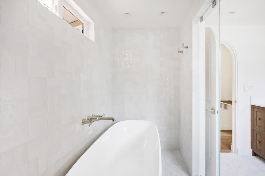 Bright white bathroom with a freestanding tub, shower area, and open door to a hallway