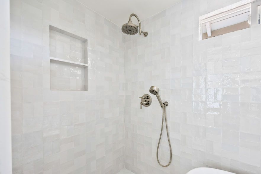White tiled walk-in shower with built-in niches and a handheld showerhead