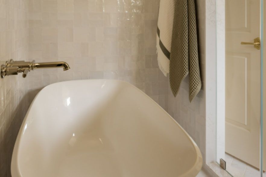 Modern bathroom with a white bathtub, brass faucet, and beige walls