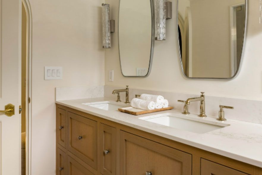 Bright bathroom vanity with double sinks, gold faucets, mirrors, and folded towels on the counter.