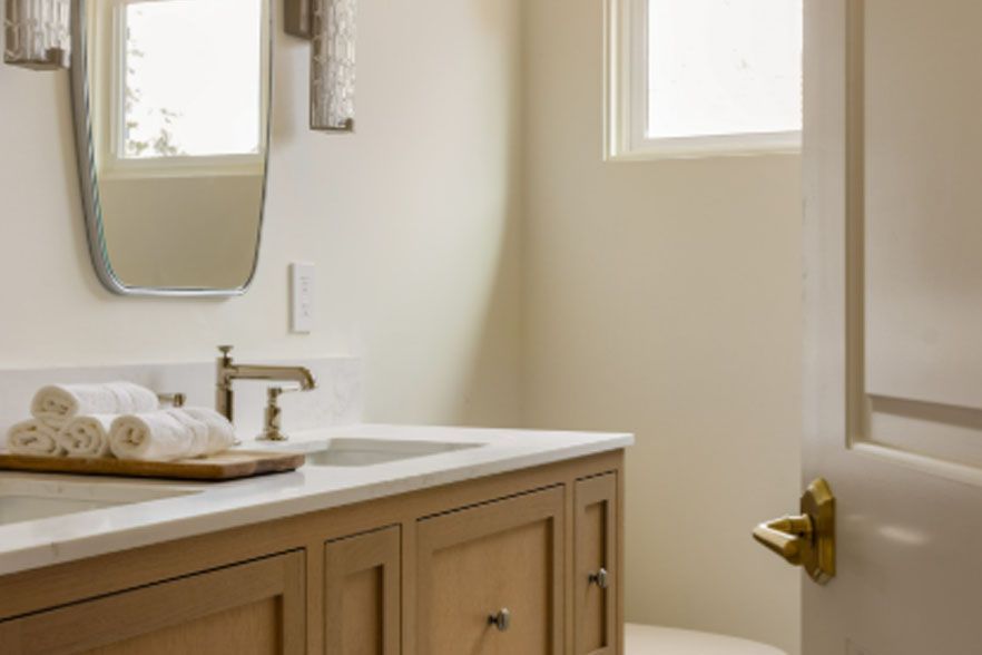 Bright bathroom with vanity, sink, mirror, and neatly folded white towels near an open door