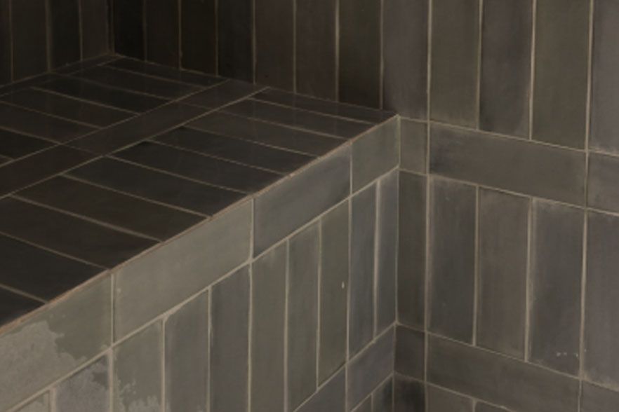 Dark gray tiled shower bench and corner wall with vertical and horizontal tiles