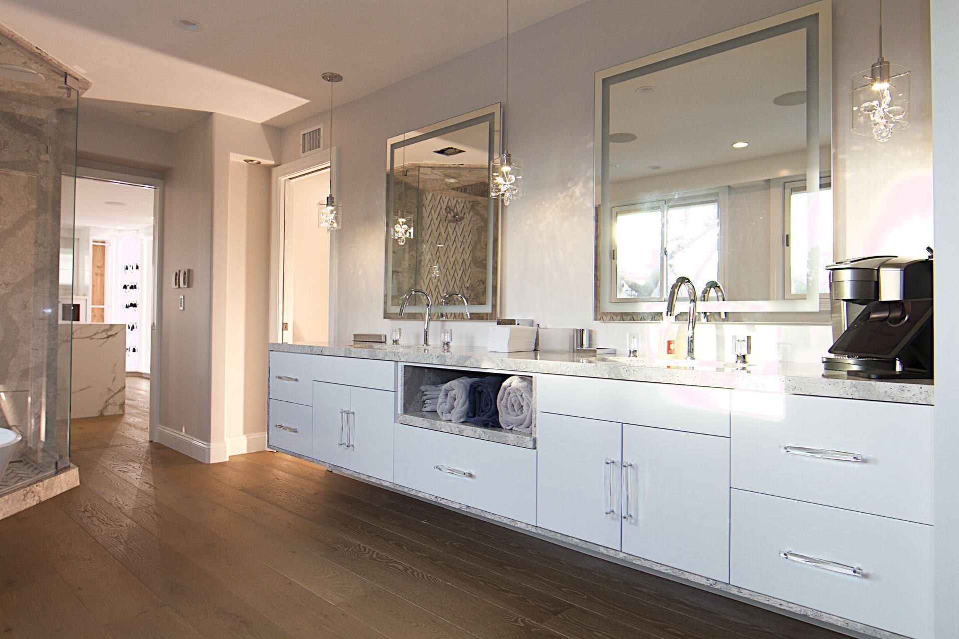 Modern bathroom with double vanity, glossy white cabinets, two large mirrors, hanging lights, and wood flooring.