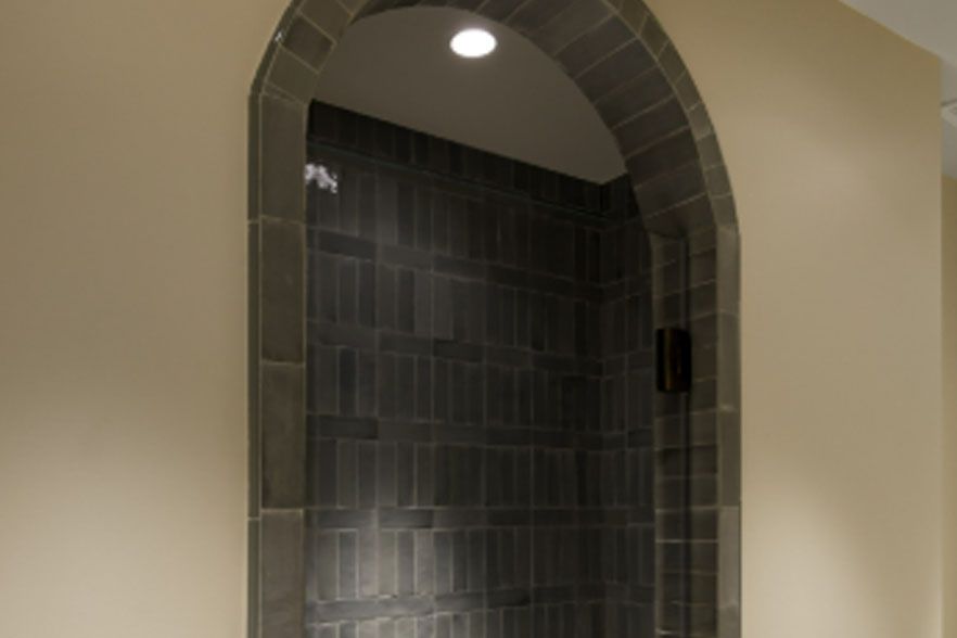 Arched doorway leading to a dark gray tiled shower alcove with a ceiling light.