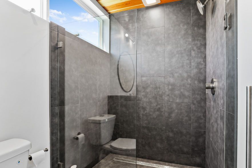 Modern gray tiled walk-in shower with a toilet and small window above the shower area