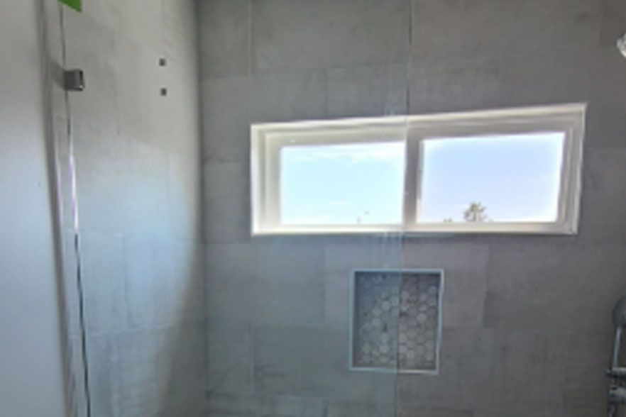 Empty tiled shower with a small frosted window and built-in niche