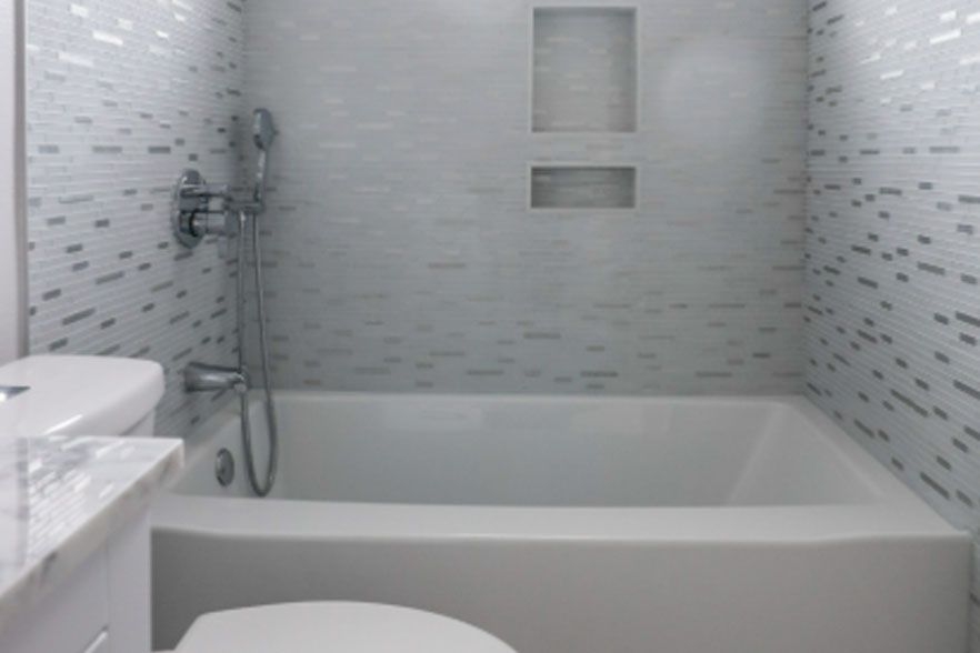 Modern white bathroom with a bathtub, tiled walls, showerhead, and small window niche