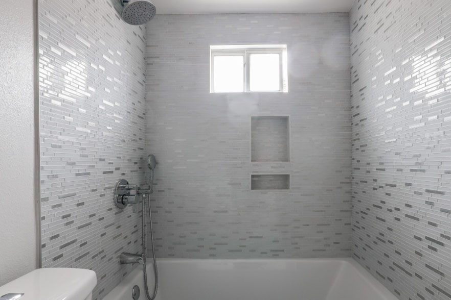 Modern white tiled bathroom with a bathtub, shower fixtures, and a small window