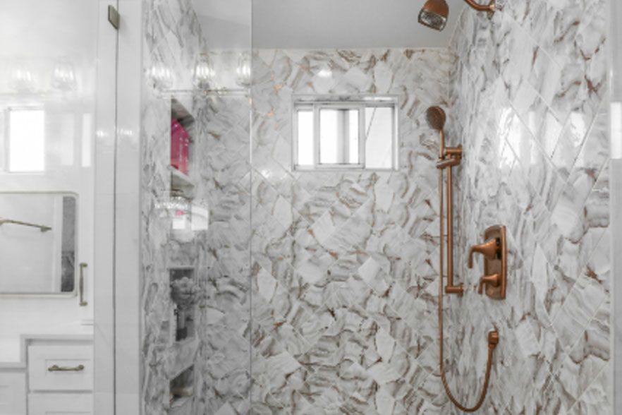 Marble-tiled bathroom shower with brass fixtures and white vanity cabinet