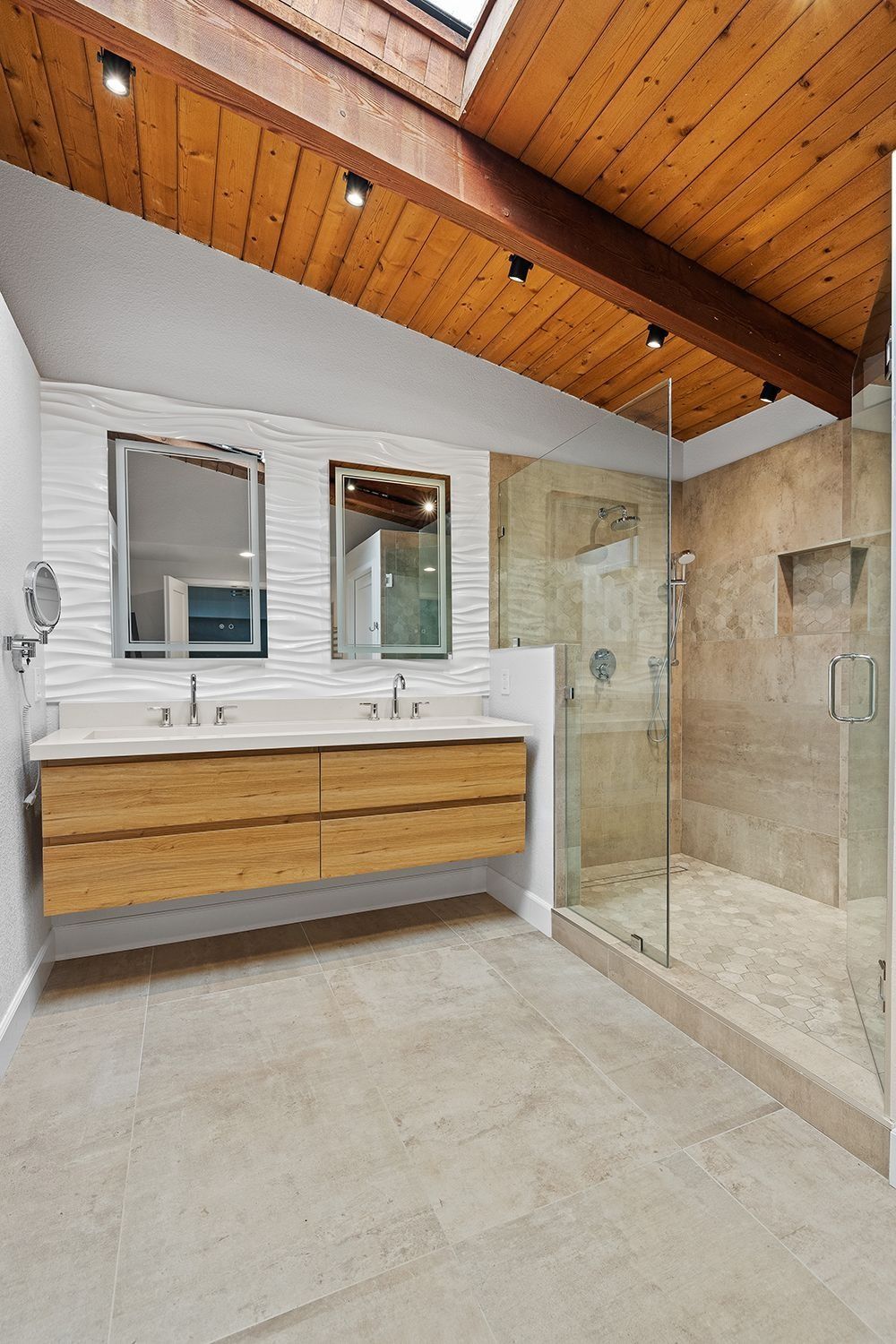A modern bathroom featuring a double wood vanity, dual mirrors, a walk-in glass shower, and a high, wood-paneled ceiling.