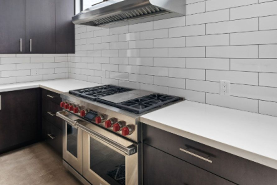 Modern kitchen with stainless steel gas range, dark cabinets, white tile backsplash, and white countertop