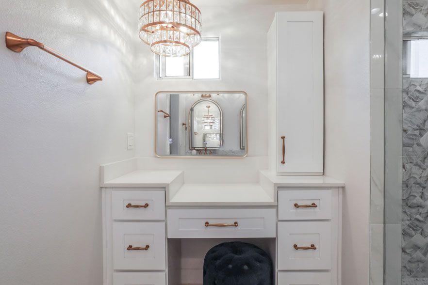 White bathroom vanity with mirror, drawers, brass accents, and a marble shower wall.
