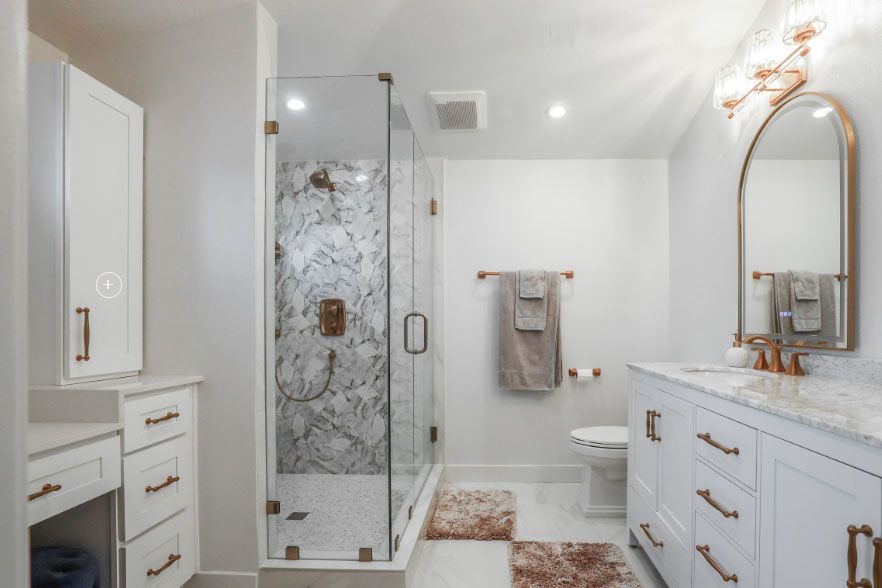 Bright white bathroom with glass shower, gold-accent vanity, and patterned rugs