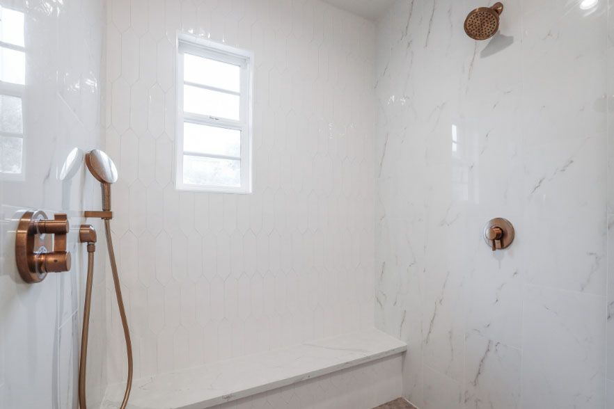 Modern tiled shower with handheld showerhead, window, bench, and two wall fixtures