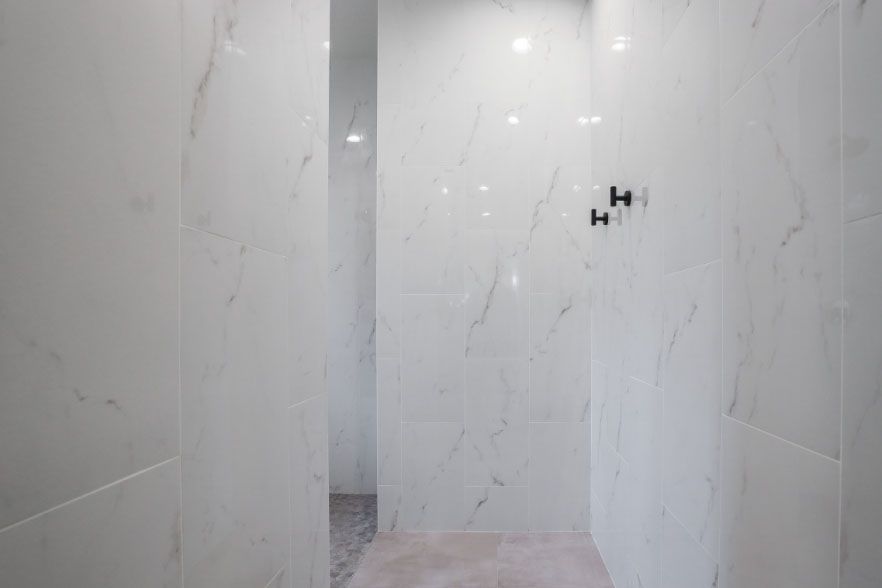 White marble-tiled shower alcove with a narrow doorway and black wall fixture