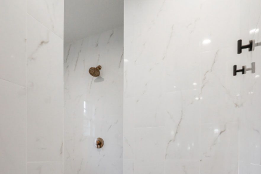 White tiled wall with two exposed plumbing holes and a shower bracket on the right