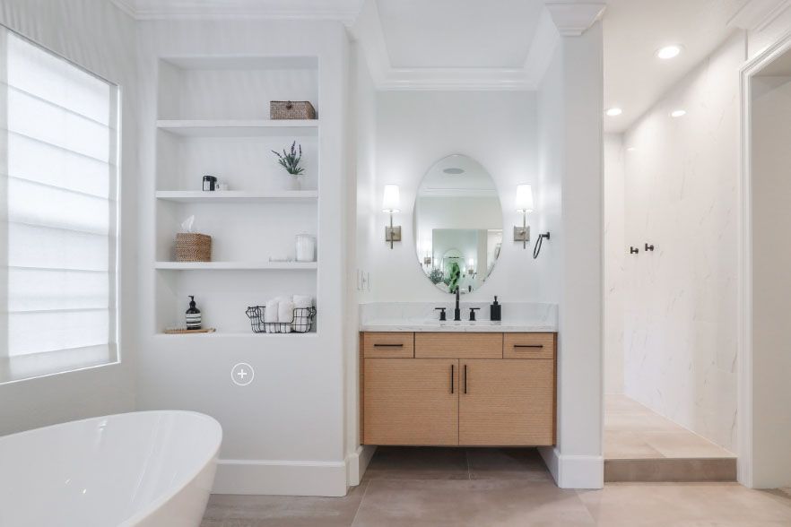 Bright modern bathroom with tub, open shelves, and wood vanity under a round mirror.