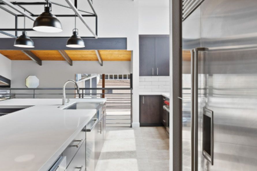 Modern stainless-steel commercial kitchen with white counters, hanging black lights, and a large fridge