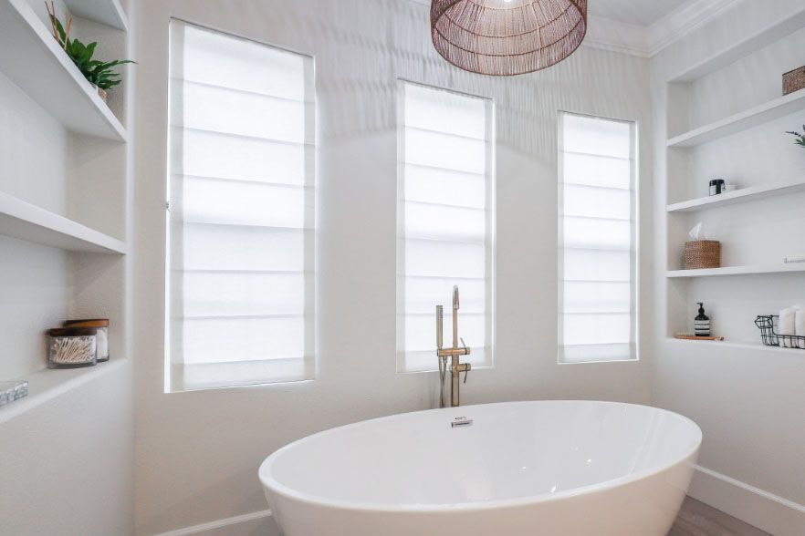 Bright white bathroom with freestanding oval tub, three windows, and built-in shelves