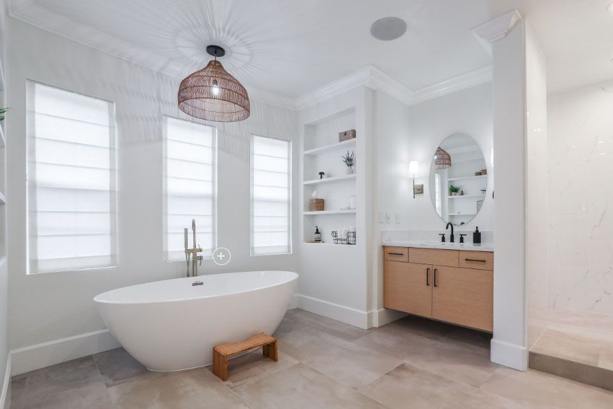 Bright modern bathroom with freestanding tub, wood vanity, large mirror, and windows with shades