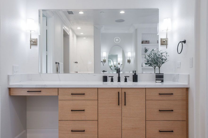 Modern bathroom vanity with large mirror, double sinks, light wood cabinets, and white countertops.