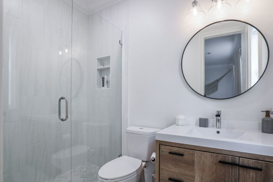 Modern white bathroom with glass shower, round mirror, and wood vanity with sink