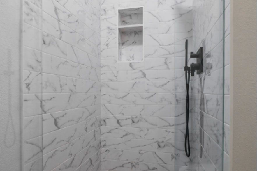 White marble-tiled shower with a recessed shelf and handheld shower head on the right.