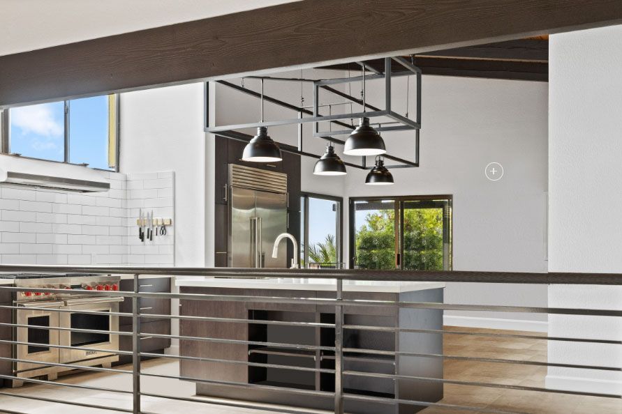 Modern kitchen interior with island, black pendant lights, stainless appliances, and metal railing
